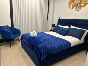 A hotel room with a large bed, a blue chair, and a decorative wall piece. - The Glamour of Shoreditch (London)