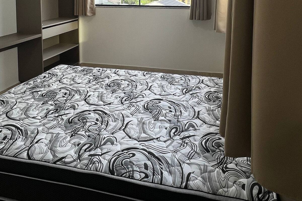 A bedroom with a bed, a wardrobe, a window with curtains, and a ceiling light.