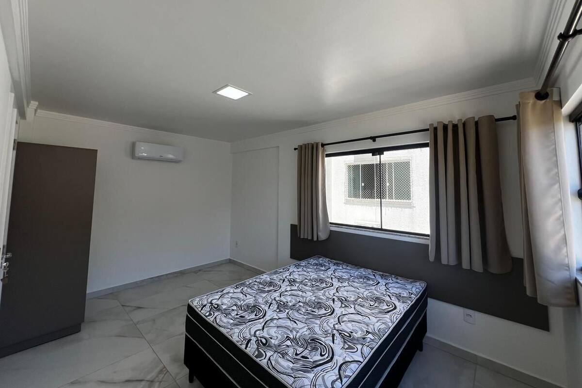 A bedroom with a bed, a window with curtains, a door, and a ceiling light.
