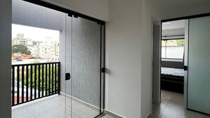 A room with a sliding glass door leading to a balcony with a black metal railing. The room has a tiled floor and a door leading to another room. - Residencial Bernardo (Bombinhas)