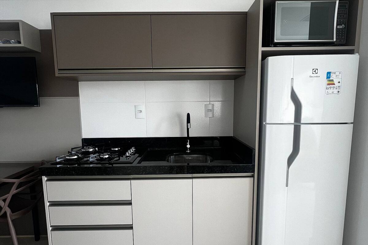 A compact kitchen with a stove, sink, and a microwave above the refrigerator.