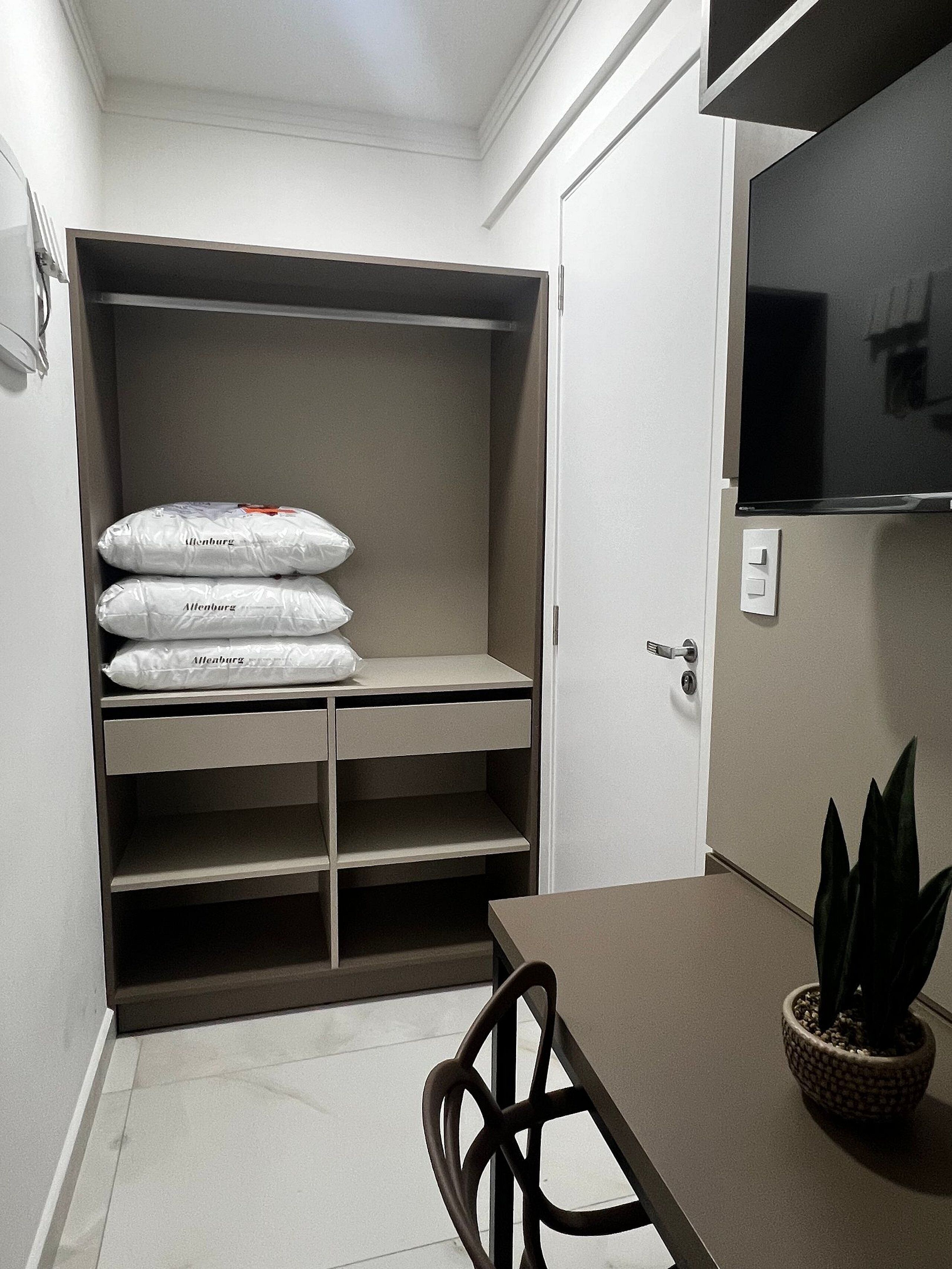 Una habitación compacta con armario empotrado que contiene tres maletas grandes, una mesa de comedor con una silla y una planta en maceta.