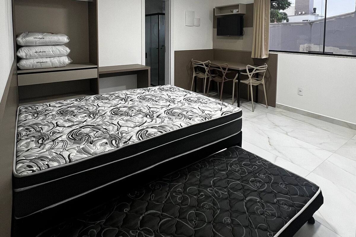A bedroom with a bed, a desk, and a chair. There is a wardrobe and a television.
