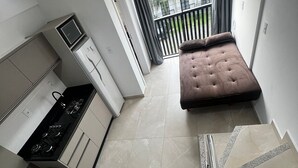 A compact living space with a kitchenette, a sofa, and a view of the outdoors. - Residencial Bernardo (Bombinhas)