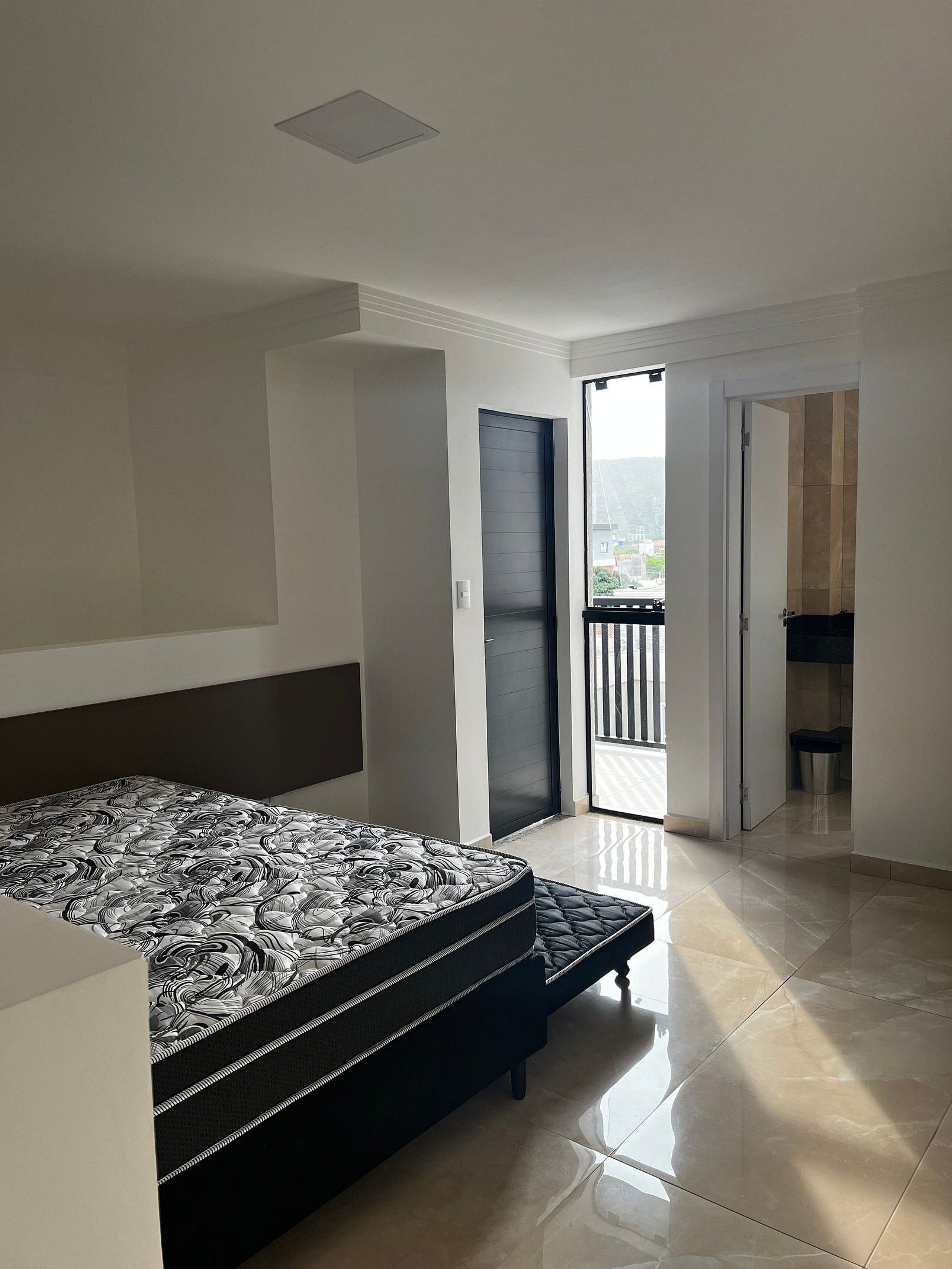 Een slaapkamer met een bed, een deur naar een balkon en uitzicht op buiten.