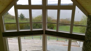 A bay window with a view of a lake and surrounding greenery. - Azure Ocean Beach House (Port McNeill)