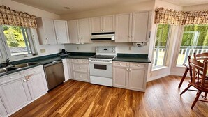A kitchen with wooden cabinets, a stove, and a sink. - Azure Ocean Beach House (Port McNeill)