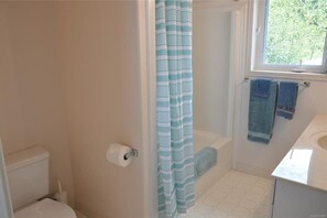 Une salle de bain comprenant des toilettes, une douche avec un rideau à rayures, une fenêtre et un porte-serviettes avec des serviettes.