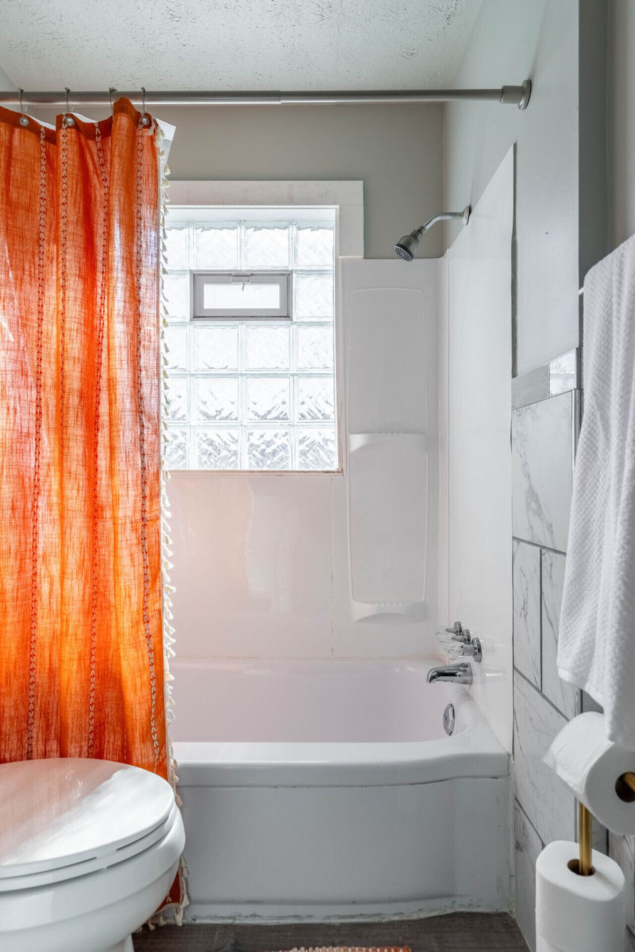 Une salle de bain avec une baignoire blanche, une fenêtre ornée d’un rideau à motifs et des toilettes.