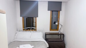 A small, neatly arranged bedroom with a single bed, a bedside table with a lamp, and a window with blinds. - Central 2-bed Apartment in Greater Manchester (Manchester)