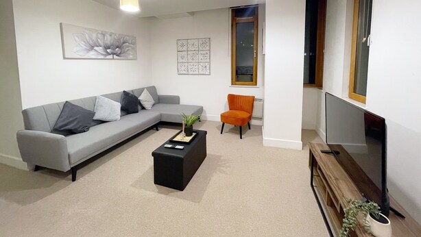 A living room with a grey sofa, an orange chair, a black coffee table, and a TV on a wooden stand. - Central 2-bed Apartment in Greater Manchester (Manchester)