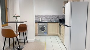 A compact kitchen with a washing machine, a refrigerator, and a dining area with two chairs. - Central 2-bed Apartment in Greater Manchester (Manchester)