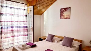 A bedroom with a wooden ceiling, a bed with white and purple bedding, a small bedside table, and a nightstand.