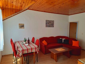 Una sala de estar acogedora con un sofá rojo, una mesa de comedor de madera con mantel a cuadros y una pequeña mesa de centro.