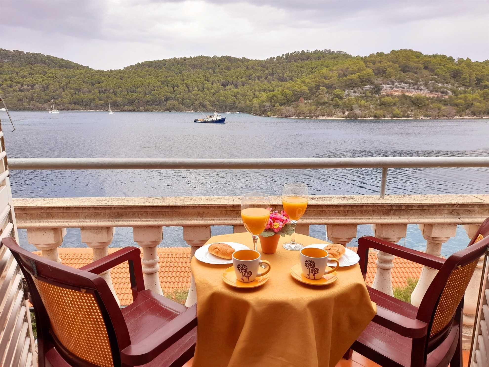 A table with a yellow tablecloth, two chairs, and a view of a lake with boats.