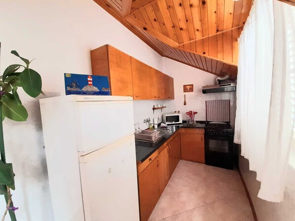 A compact kitchen with wooden cabinets, a white refrigerator, a microwave, and a stove.