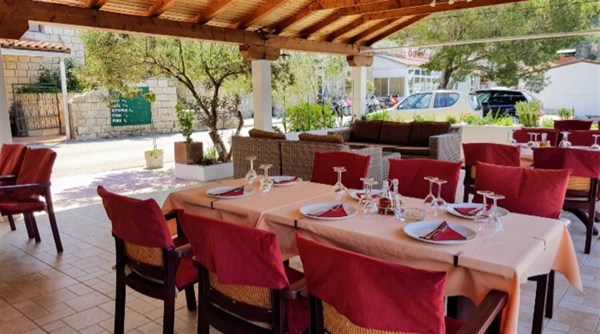 An outdoor restaurant with tables set for dining, covered by a wooden pergola.