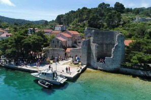 Uma vila costeira com uma muralha de pedra histórica, um cais com um barco e edifícios com telhados vermelhos.