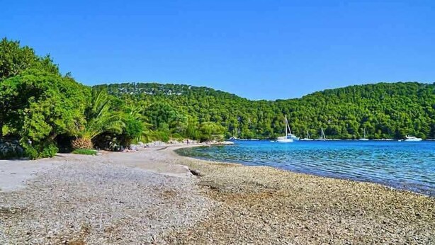 A beach with pebbles, boats, and dense green hills.