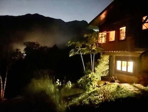 Una casa con una ventana iluminada y vistas a montañas al fondo.
