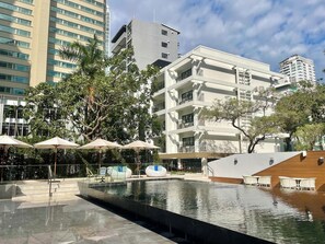 A modern hotel with a pool area, outdoor seating, and a view of surrounding buildings. - Floral Court Hotel and Residence (Bangkok)