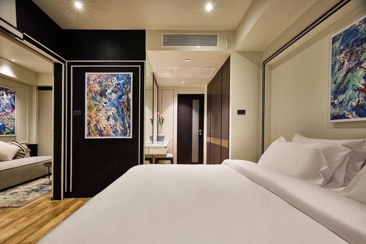 A modern hotel room with a large bed, a desk, and artwork on the walls.