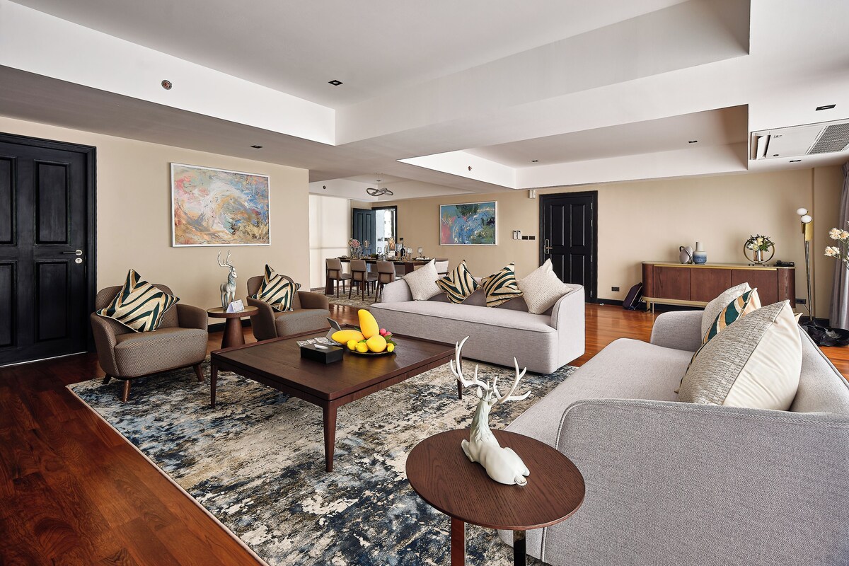 A spacious living room with a large sofa, a coffee table, and a dining area in the background.