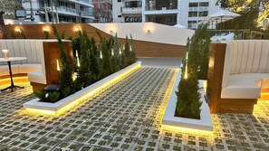 An outdoor seating area with modern furniture and a patterned floor, surrounded by greenery and illuminated by ambient lighting. - Floral Court Hotel and Residence (Bangkok)
