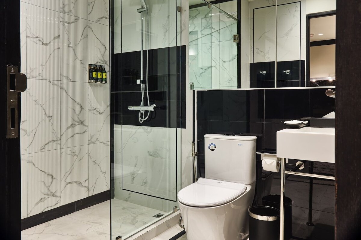 A modern bathroom with a glass-enclosed shower, a white toilet, and a black and white tiled wall.