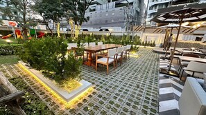 An outdoor seating area with tables and chairs, surrounded by greenery and decorative lights. - Floral Court Hotel and Residence (Bangkok)