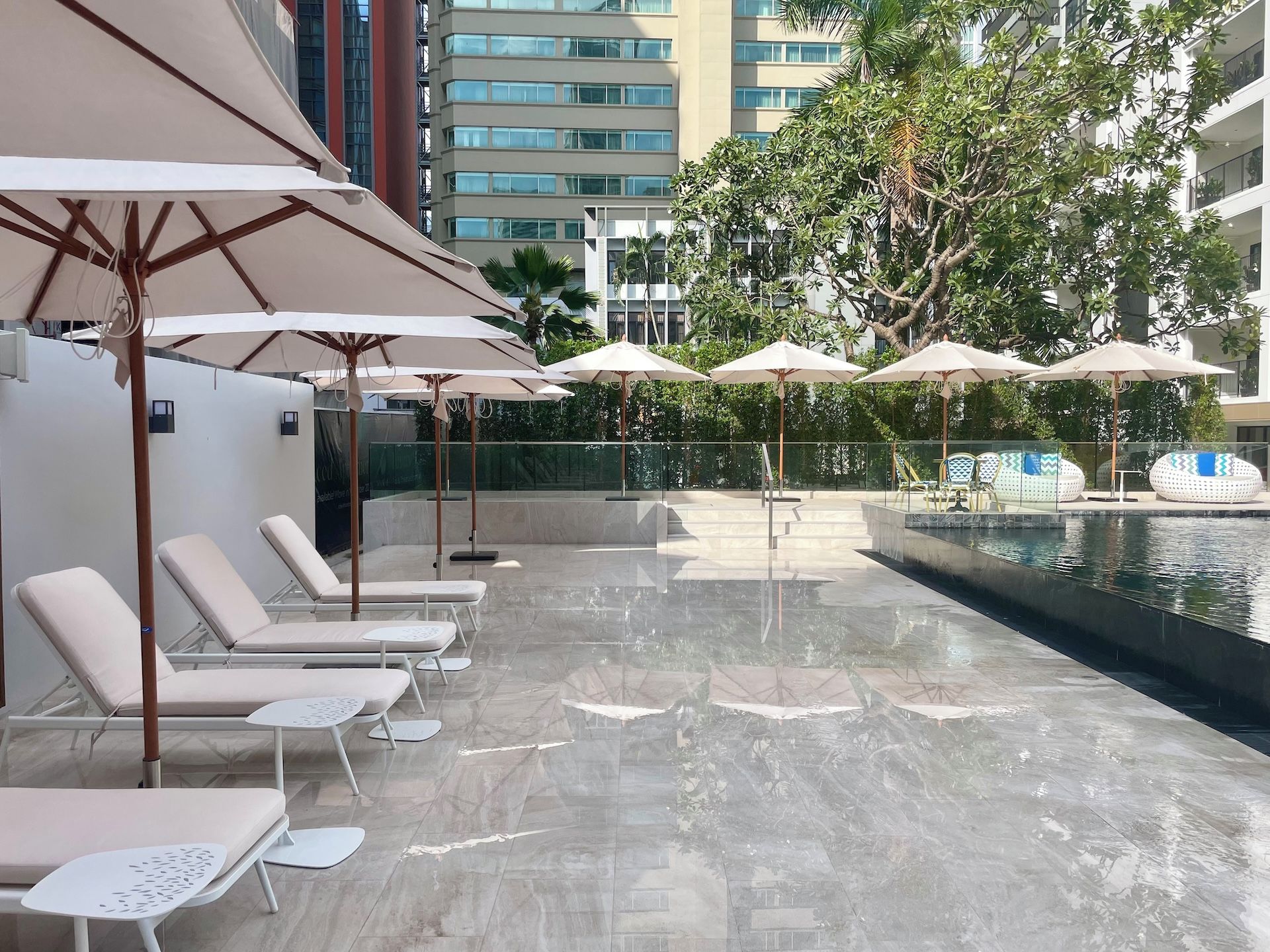 A poolside area with lounge chairs and umbrellas, a water feature, and a view of a modern building.