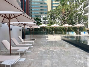A poolside area with lounge chairs and umbrellas, a water feature, and a view of a modern building. - Floral Court Hotel and Residence (Bangkok)