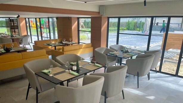 A modern dining area with tables and chairs, large windows, and a view of the outdoors. - Floral Court Hotel and Residence (Bangkok)