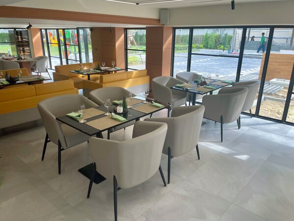 A modern dining area with tables and chairs, large windows, and a view of the outdoors. - Floral Court Hotel and Residence (Bangkok)