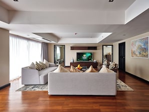A modern living room with a grey sofa, a flat-screen TV, and a wooden floor. - Floral Court Hotel and Residence (Bangkok)