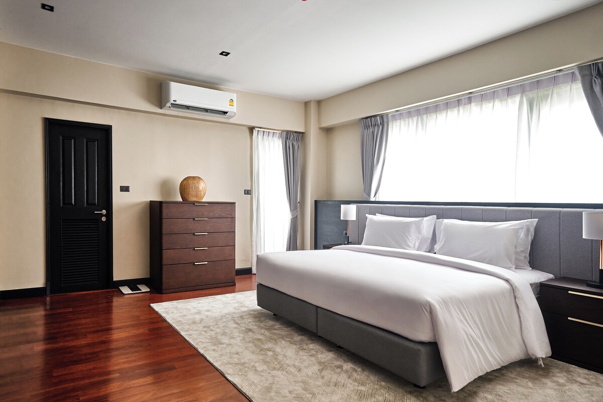 A modern bedroom with a large bed, a dresser, and an air conditioning unit.