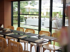 A dining area with tables and chairs, large windows, and outdoor seating visible through the glass. - Floral Court Hotel and Residence (Bangkok)
