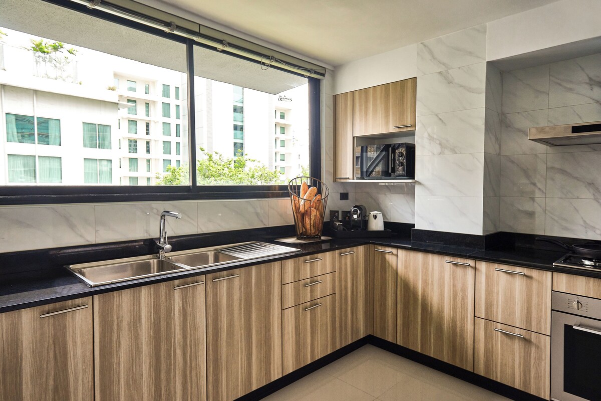 A modern kitchen with wooden cabinets, a black countertop, a stainless steel sink, and a window overlooking a building.