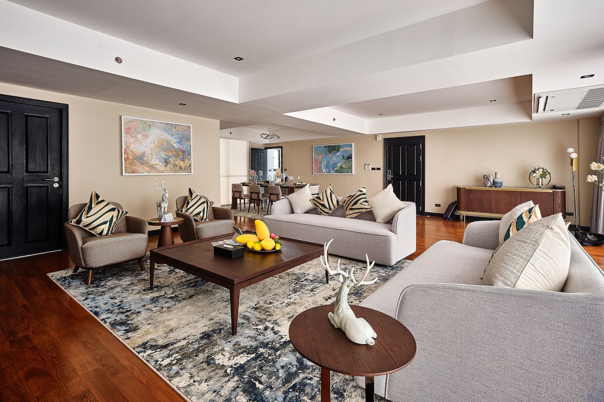 A spacious living room with a large sofa, a coffee table, and a dining area in the background.