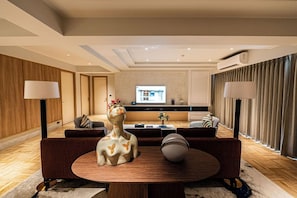 A modern living room with a round coffee table, sofas, a decorative giraffe sculpture, and a television in the background. - Floral Court Hotel and Residence (Bangkok)