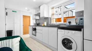 Een moderne keuken met witte kasten, een ingebouwde oven, een magnetron en een wasmachine.