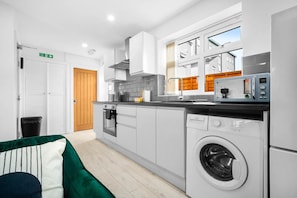 A modern kitchen with white cabinets, a built-in oven, a microwave, and a washing machine. - Luxury 3 Bedroom Apartment- Terrace (Birmingham)