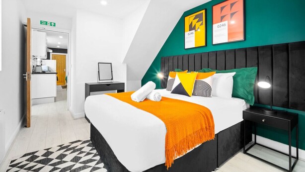 Een moderne hotelkamer met een groot bed, nachtkastje, bureau en een groene accentmuur.