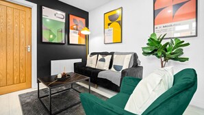 Een moderne woonkamer met een zwart-wit sofa, een groene fauteuil en een salontafel. Er hangen abstracte kunstwerken aan de muur en staat een potplant.