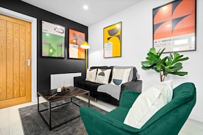A modern living room with a black and white sofa, a green armchair, and a coffee table. There are abstract art pieces on the walls and a potted plant. - Luxury 3 Bedroom Apartment- Terrace (Birmingham)