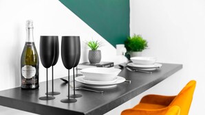 Een moderne eettafel met een fles Prosecco, twee zwarte wijnglazen en witte borden.