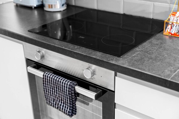 A kitchen with a black induction cooktop, stainless steel oven, and a white countertop.