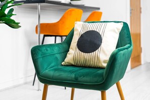A green armchair with a black and white pillow, a wooden floor, and a bright orange chair in the background.