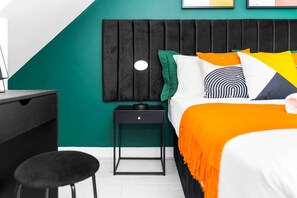 A bedroom with a black headboard, a bed with an orange blanket, and a small bedside table with a lamp.