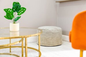 A corner of a room with a round glass table, a beige ottoman, and a potted plant. - Luxury Apartment  - WiFi (Birmingham)